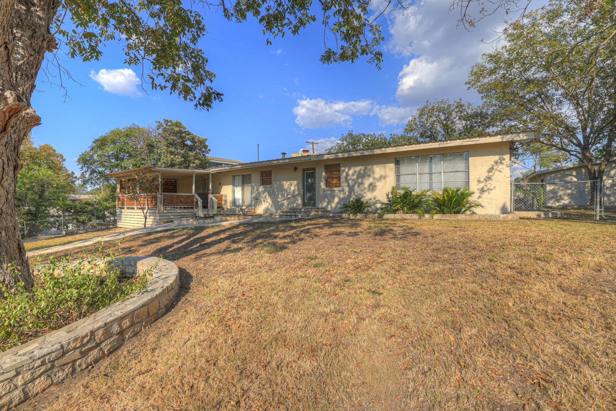 Residential house with a large backyard, trees, and a clear blue sky with a few clouds.