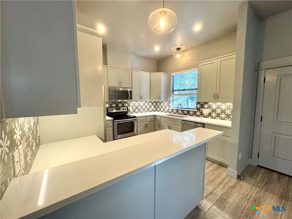 Modern kitchen with white cabinets, black and white patterned tile backsplash, stainless steel appliances, a window above the sink, and a white countertop.