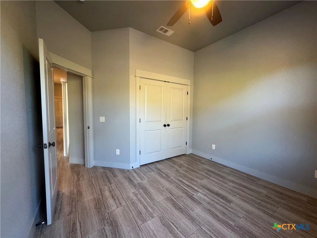 Empty bedroom with gray walls, a closet with double doors, wood-look flooring, and a ceiling fan with a light
