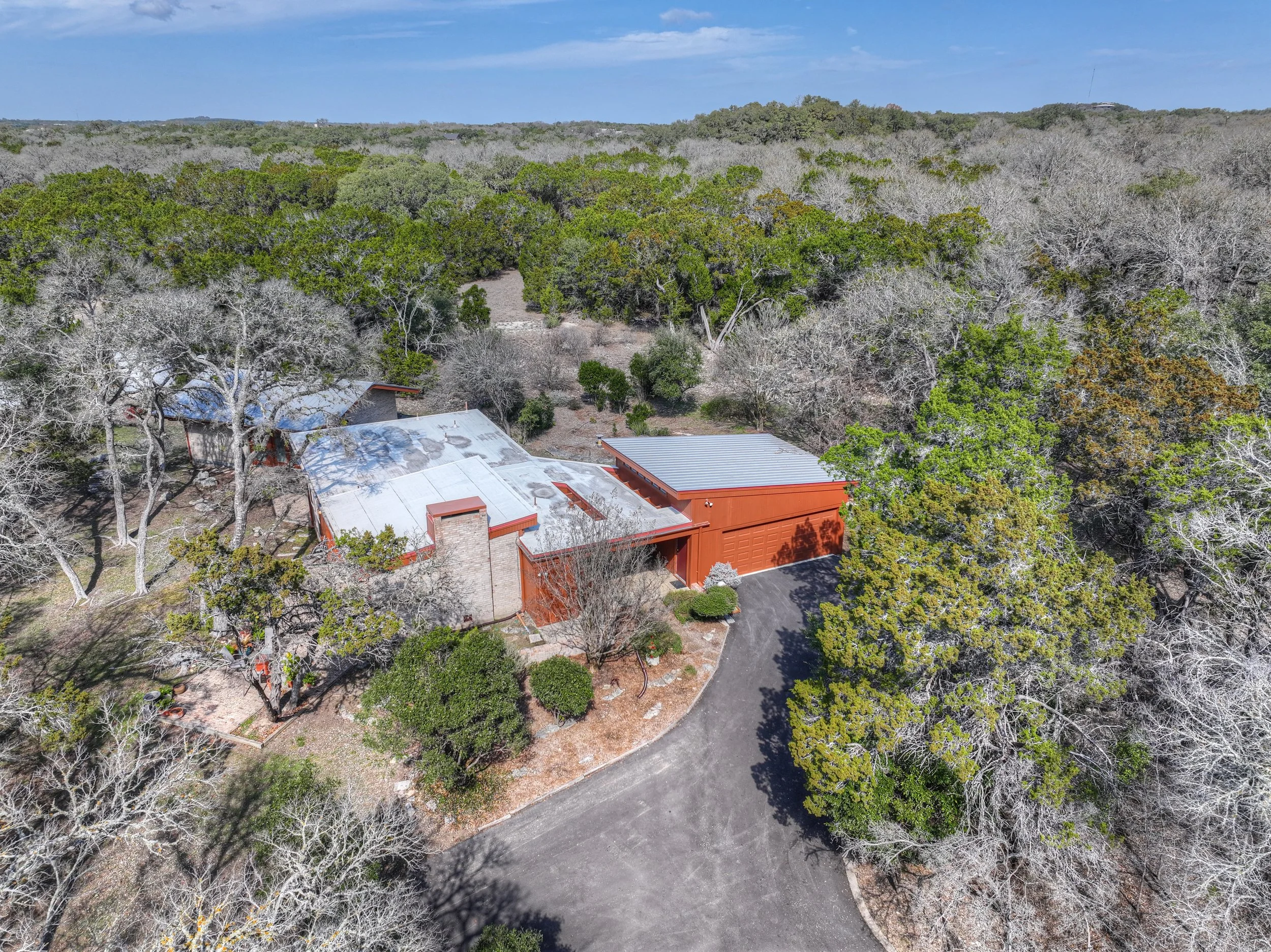 Aerial view of a house surrounded by trees in a wooded area on a clear day.