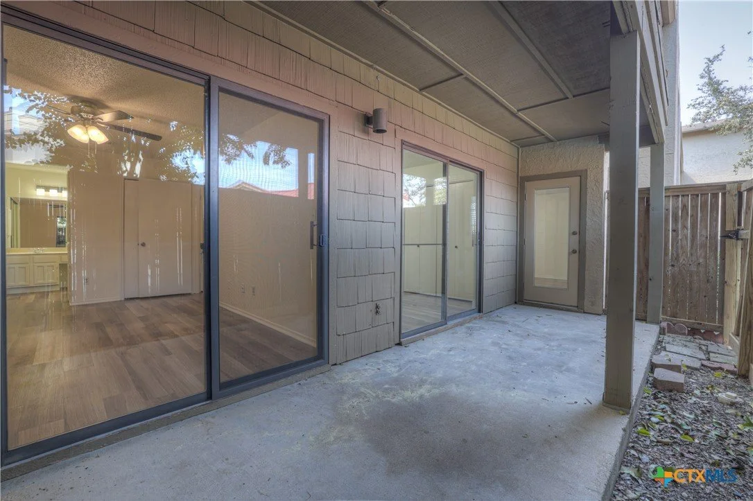 Back patio area with sliding glass doors leading into a house, concrete floor, and a wooden privacy fence.