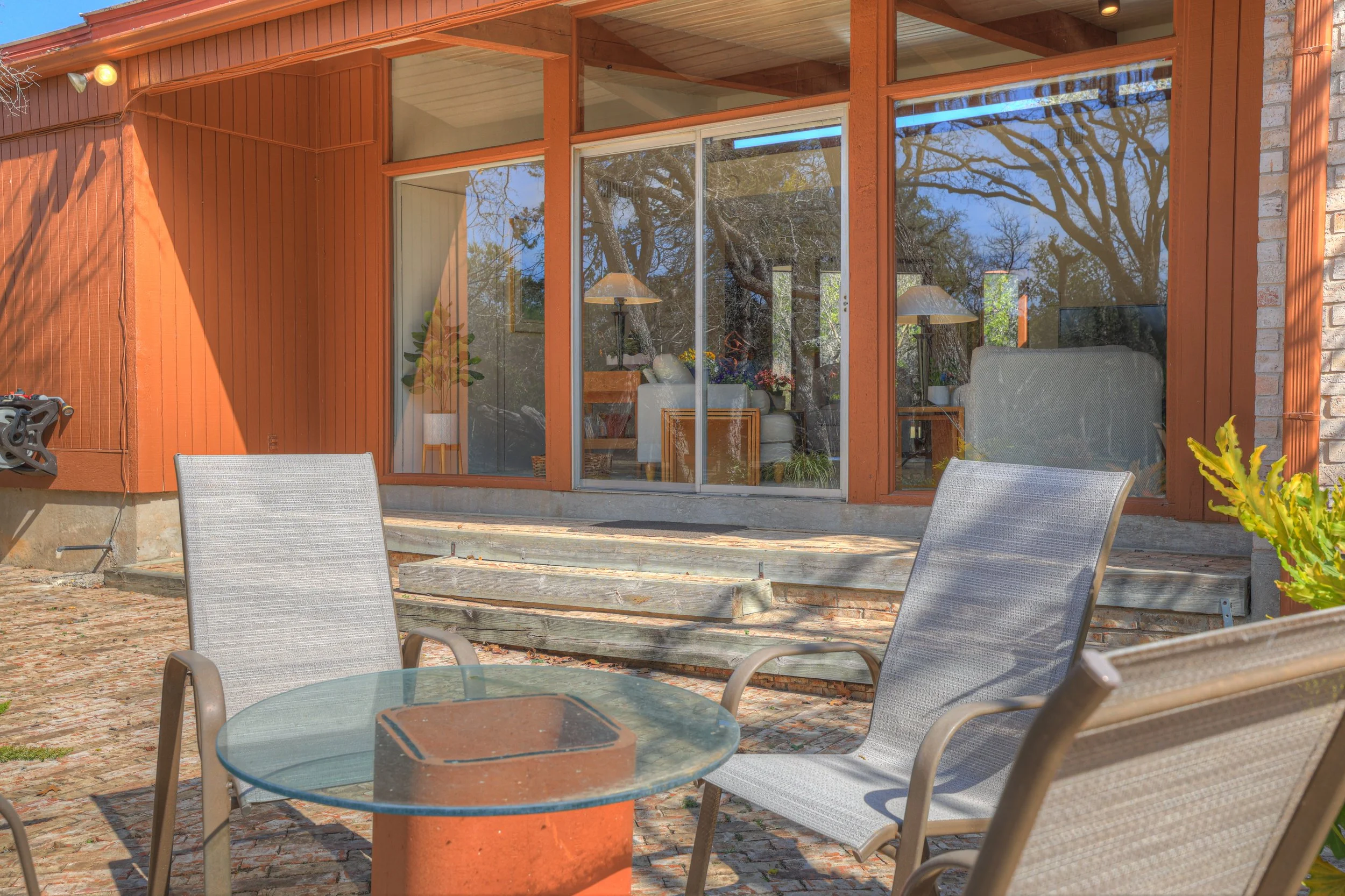 Outdoor patio with glass-top table and four mesh chairs in front of a house with large windows and wooden siding