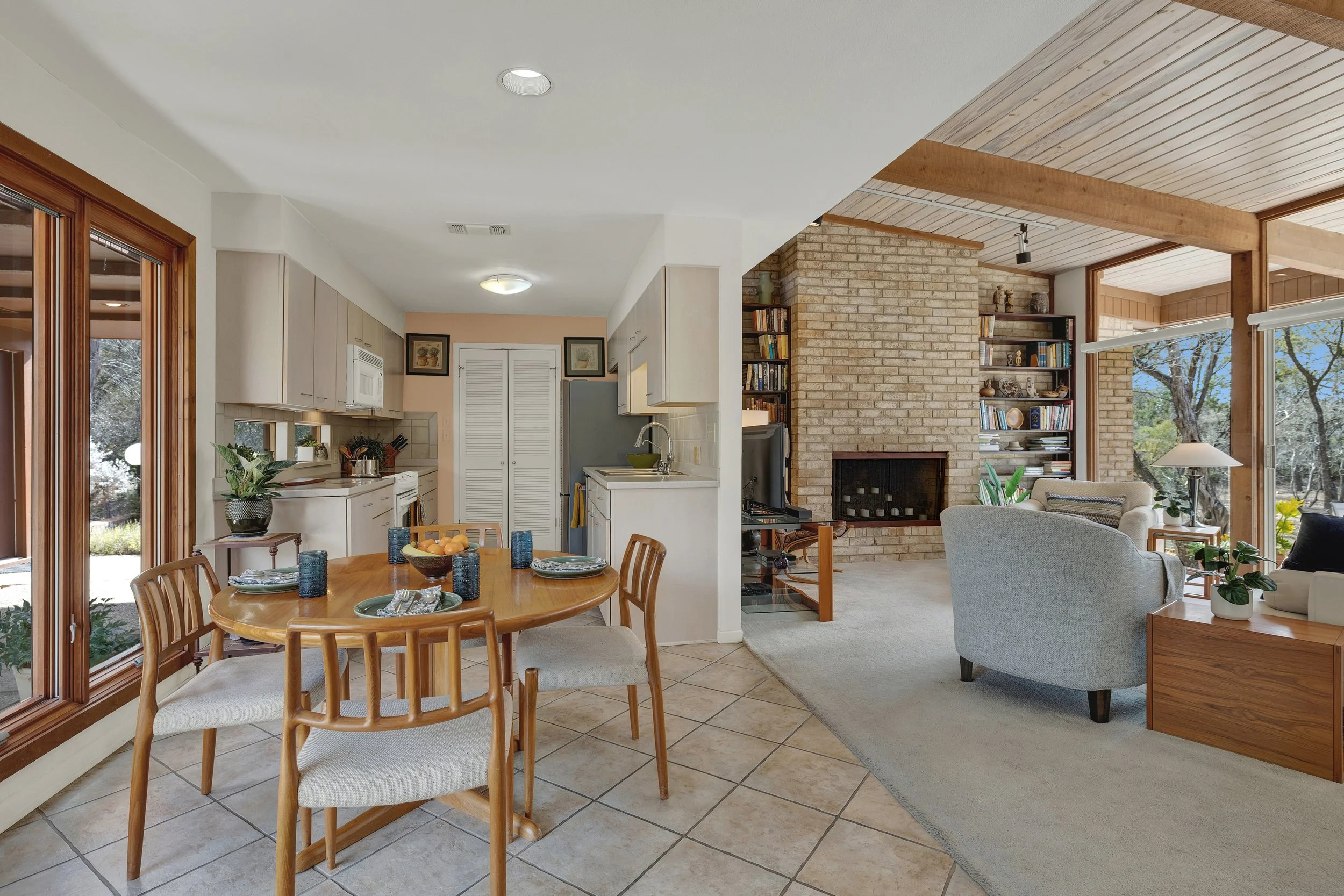 Open-concept dining and living room with large windows, brick fireplace, and bookshelves.