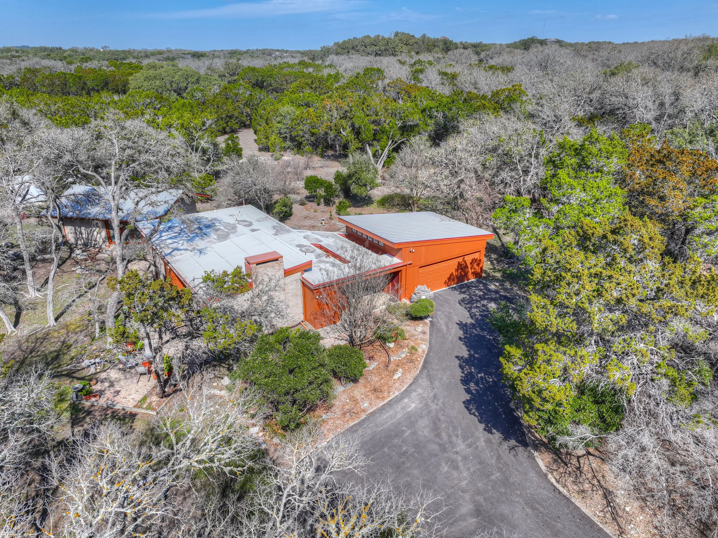 Aerial view of a house surrounded by trees and a curved driveway, with a dense forest in the background.