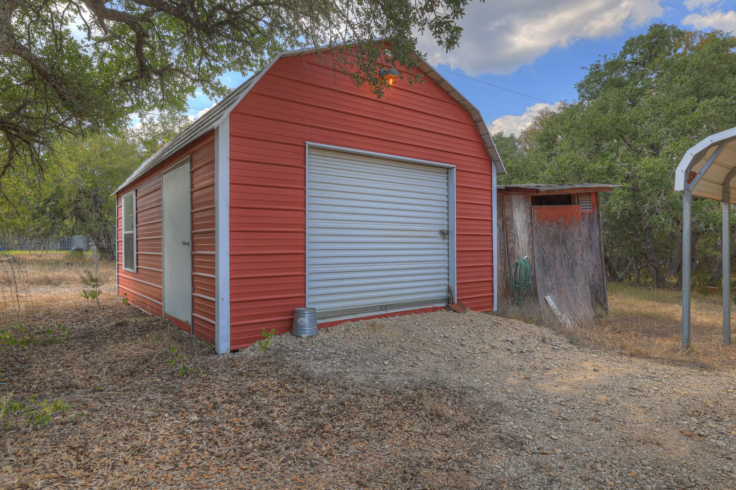 Red metal shed with a white roll-up door and side window, surrounded by trees and dry ground with scattered leaves.