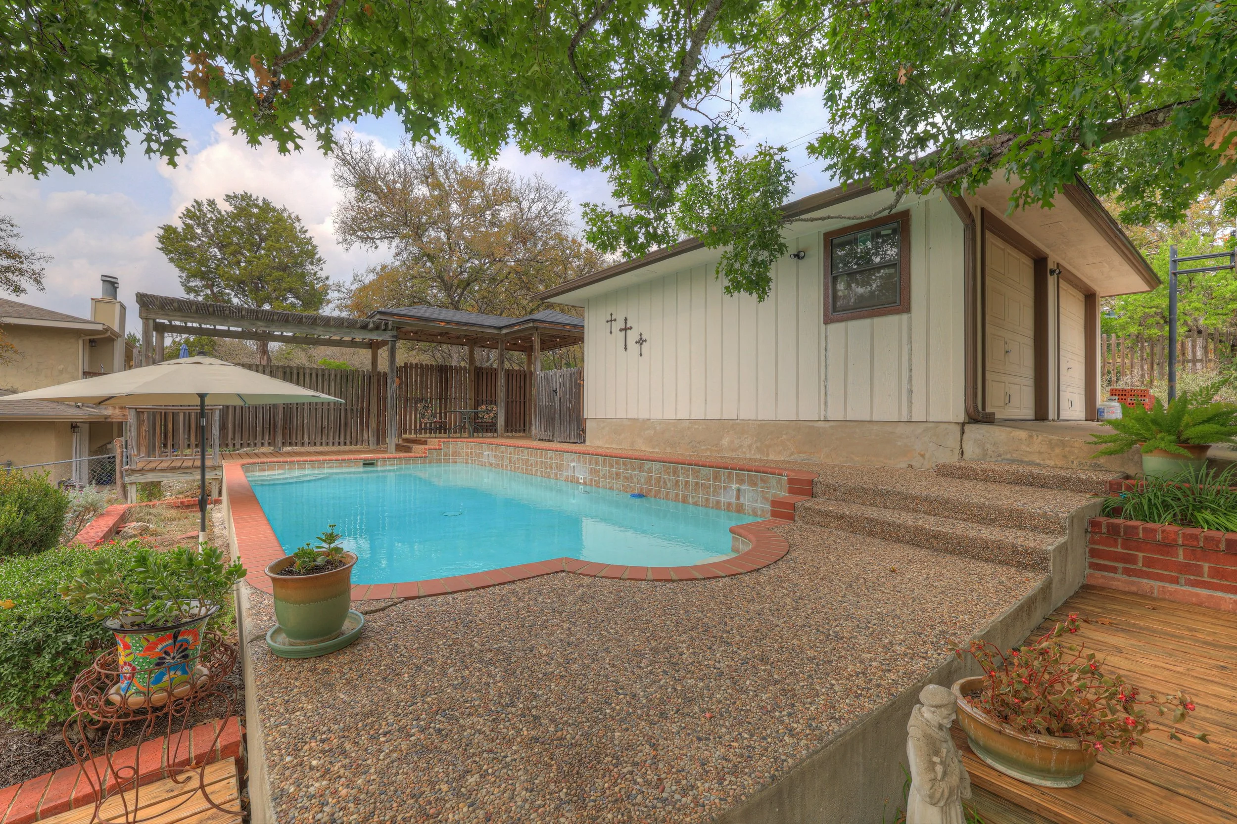 Backyard with a swimming pool, potted plants, trees, and a small house or shed with a slide and outdoor furniture.