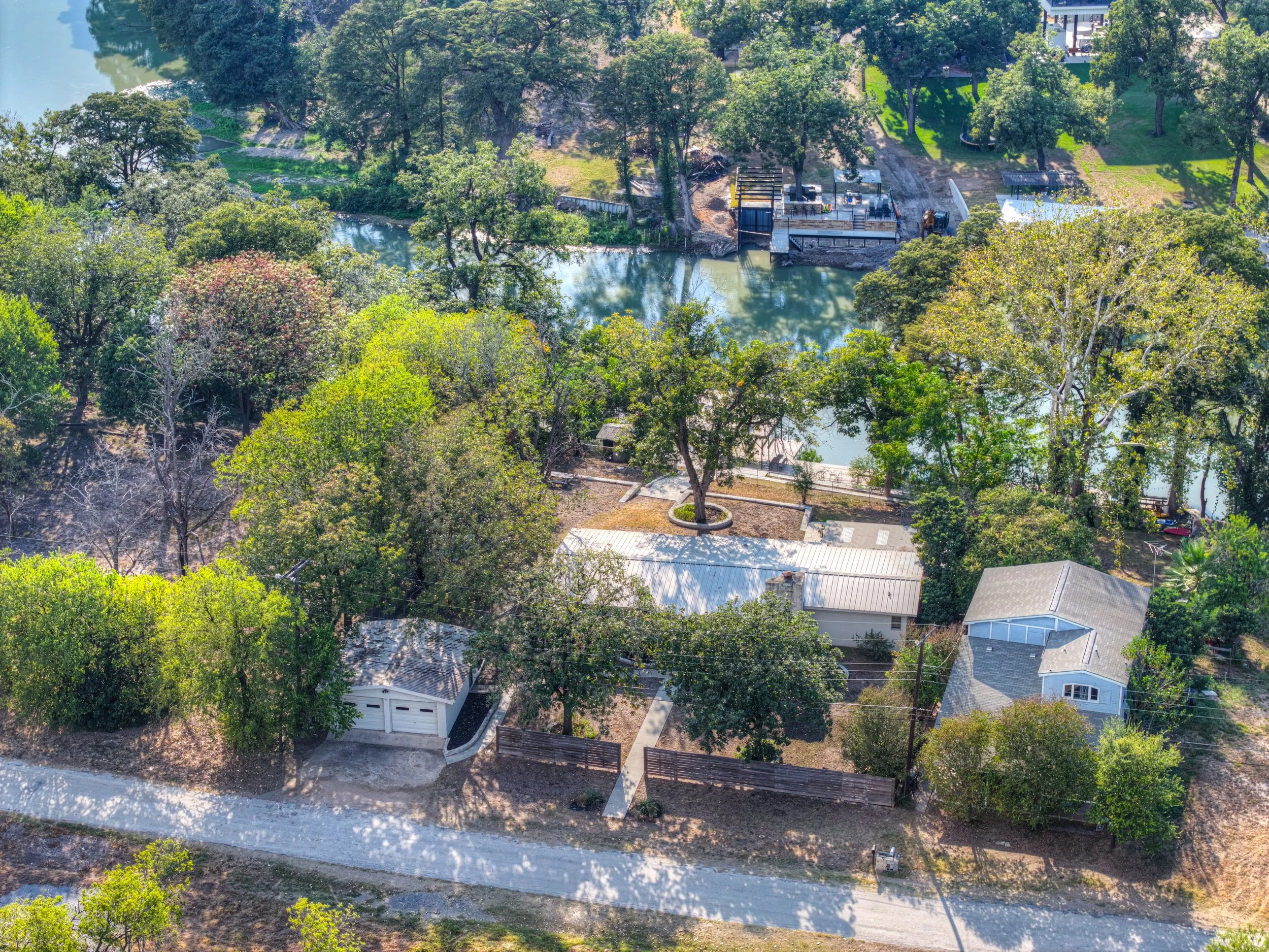 Aerial view of a suburban neighborhood near a river, with trees, houses, and a small boat dock.