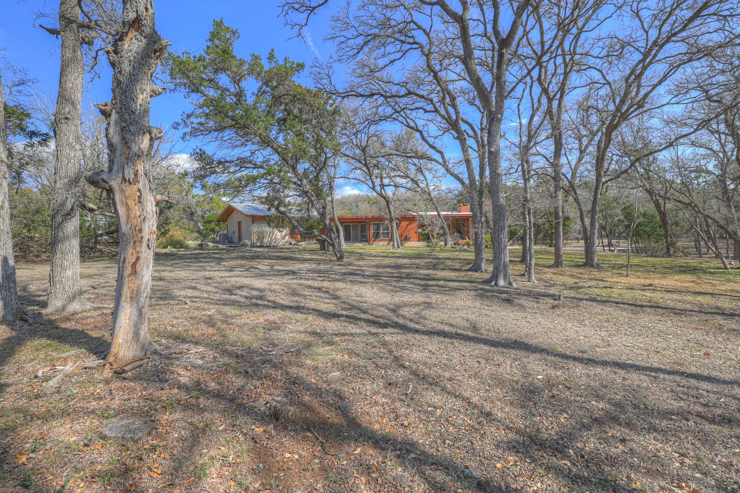 A house in a wooded area with tall trees and a clear blue sky.