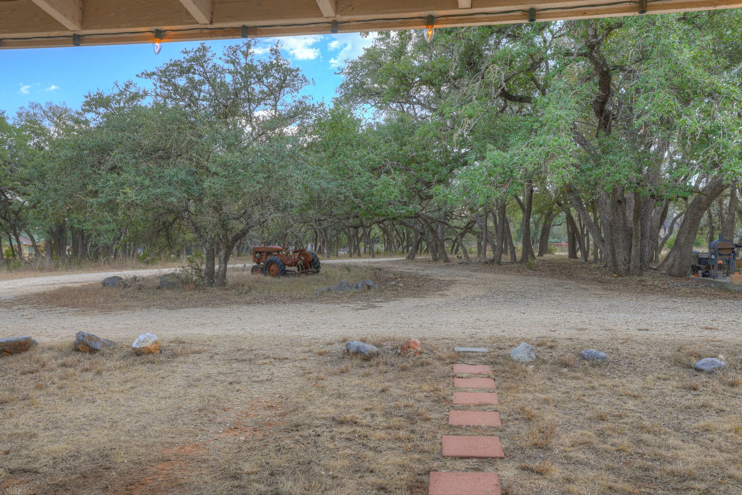 View of a yard with a red brick pathway, trees, and an old tractor in the background.