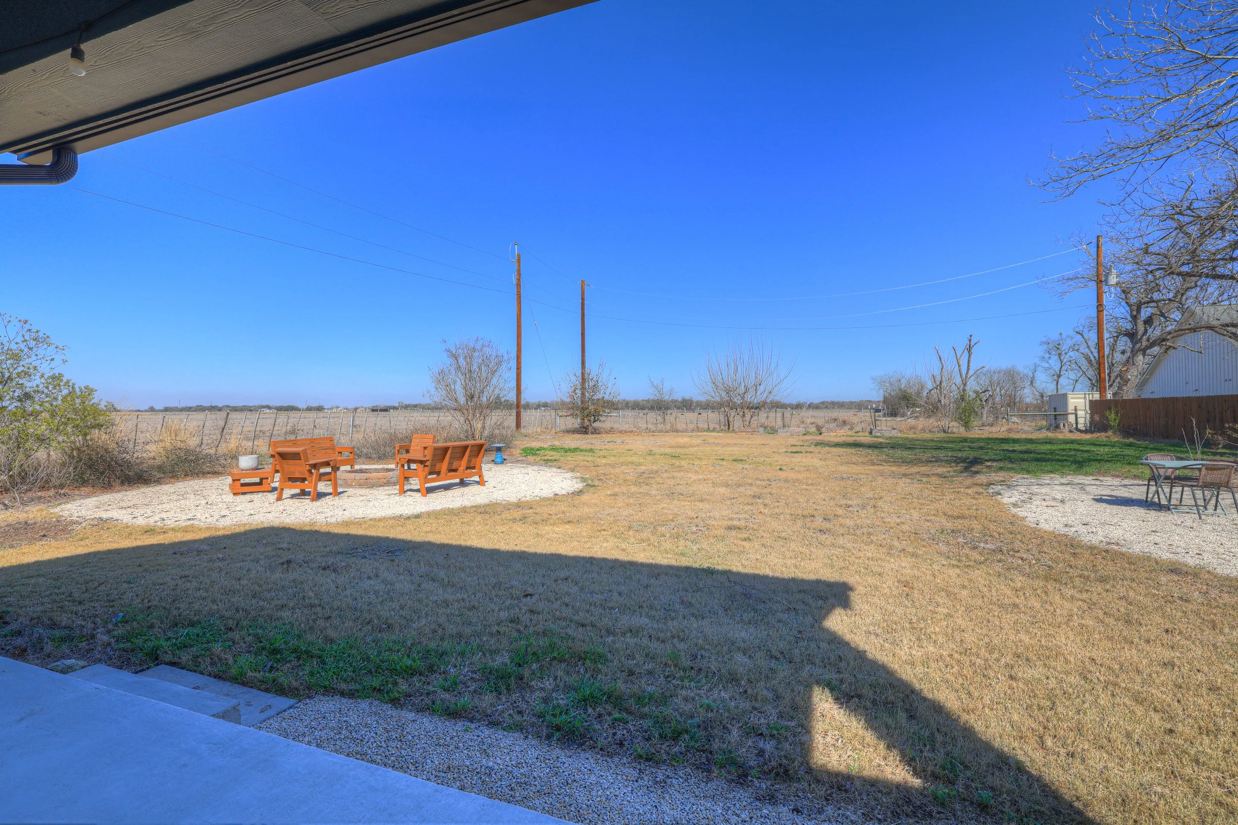 Backyard view with lawn, outdoor seating, and a clear blue sky.