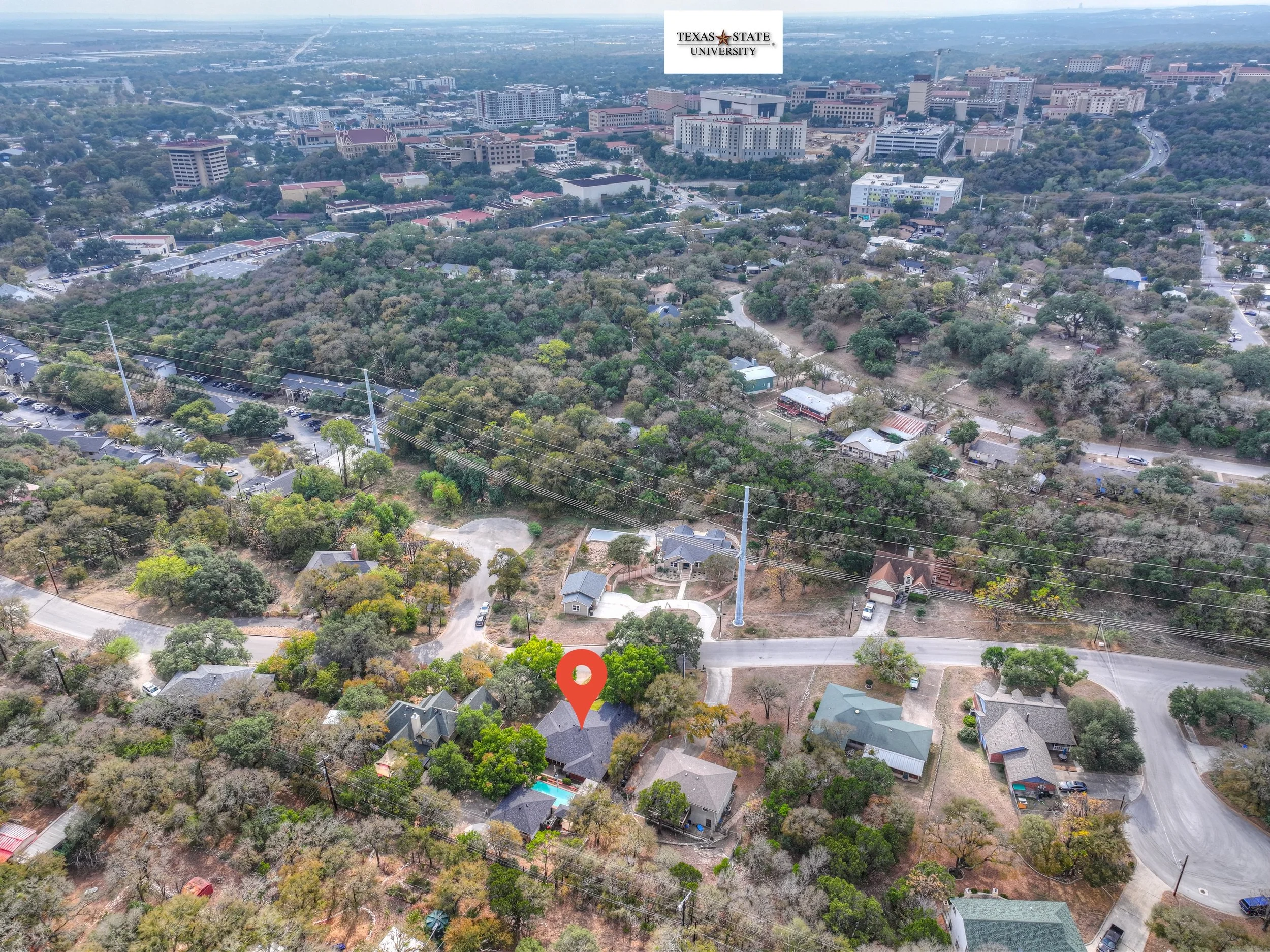 Aerial view of a neighborhood with trees, houses, and roads in Austin, Texas, with Texas State University buildings visible in the distance.