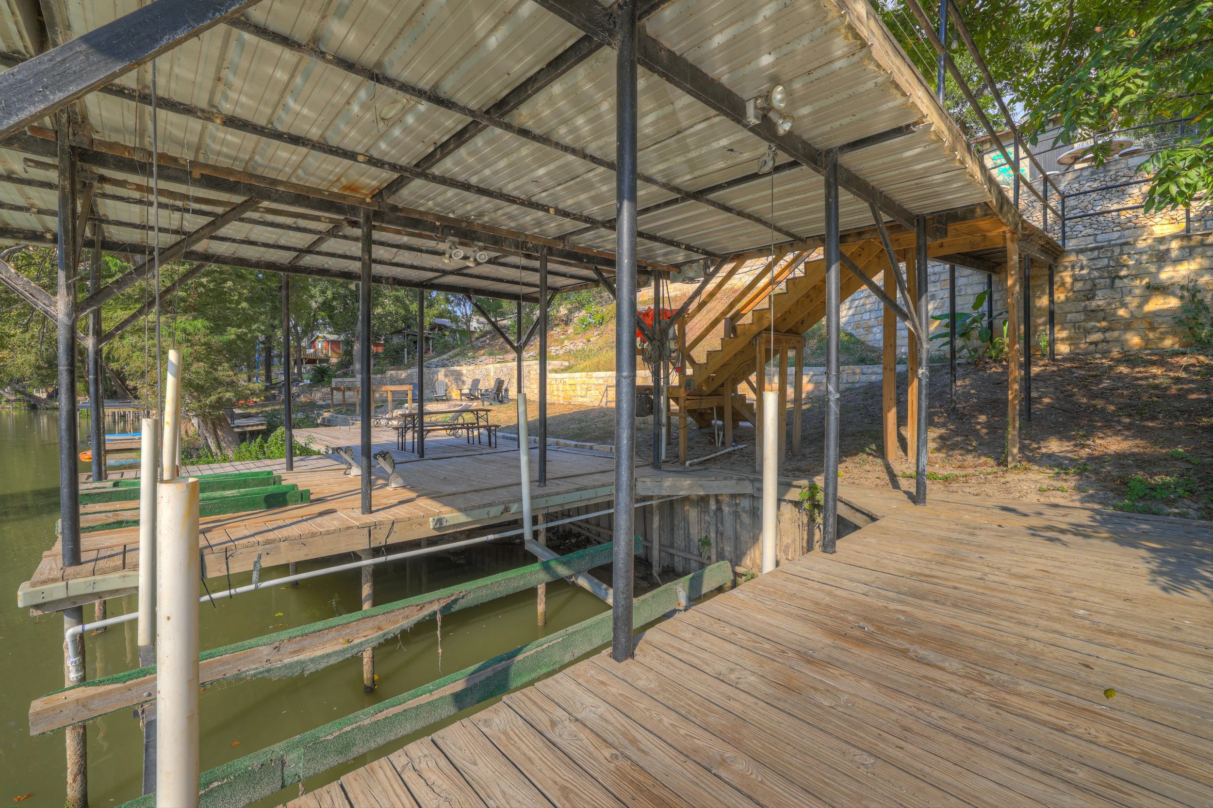 Under construction wooden dock and staircase next to a body of water with trees and outdoor furniture in the background.