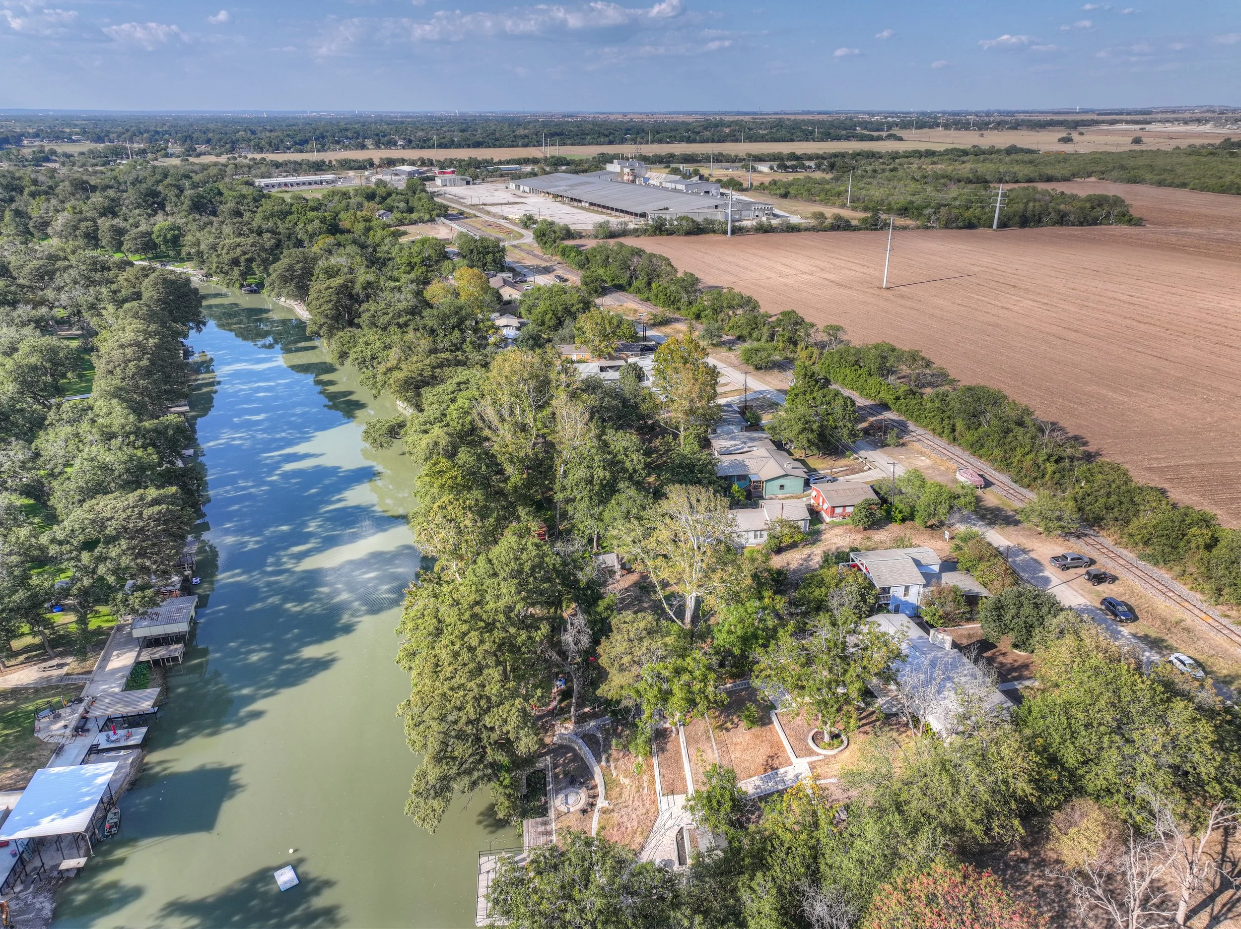 Aerial view of a park with a narrow lake lined by trees, residential houses along the shore, and farmland in the background.