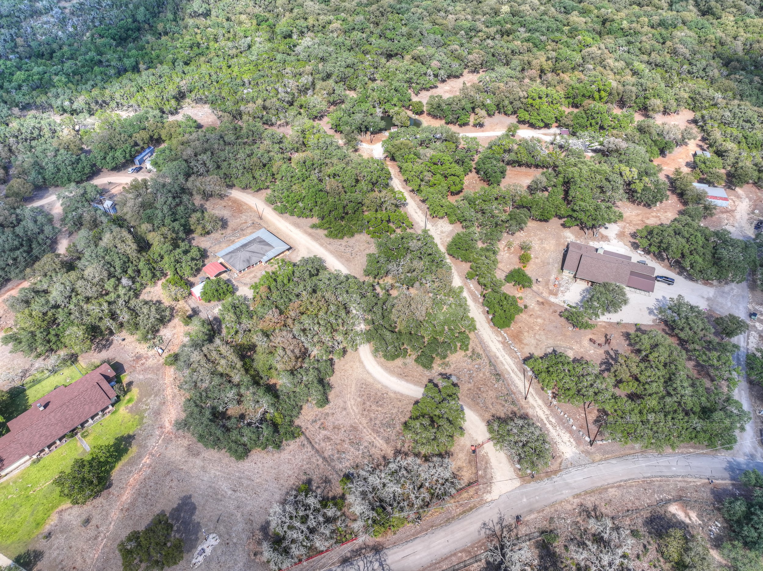 Aerial view of a rural area with several houses, dirt roads, and dense green trees.