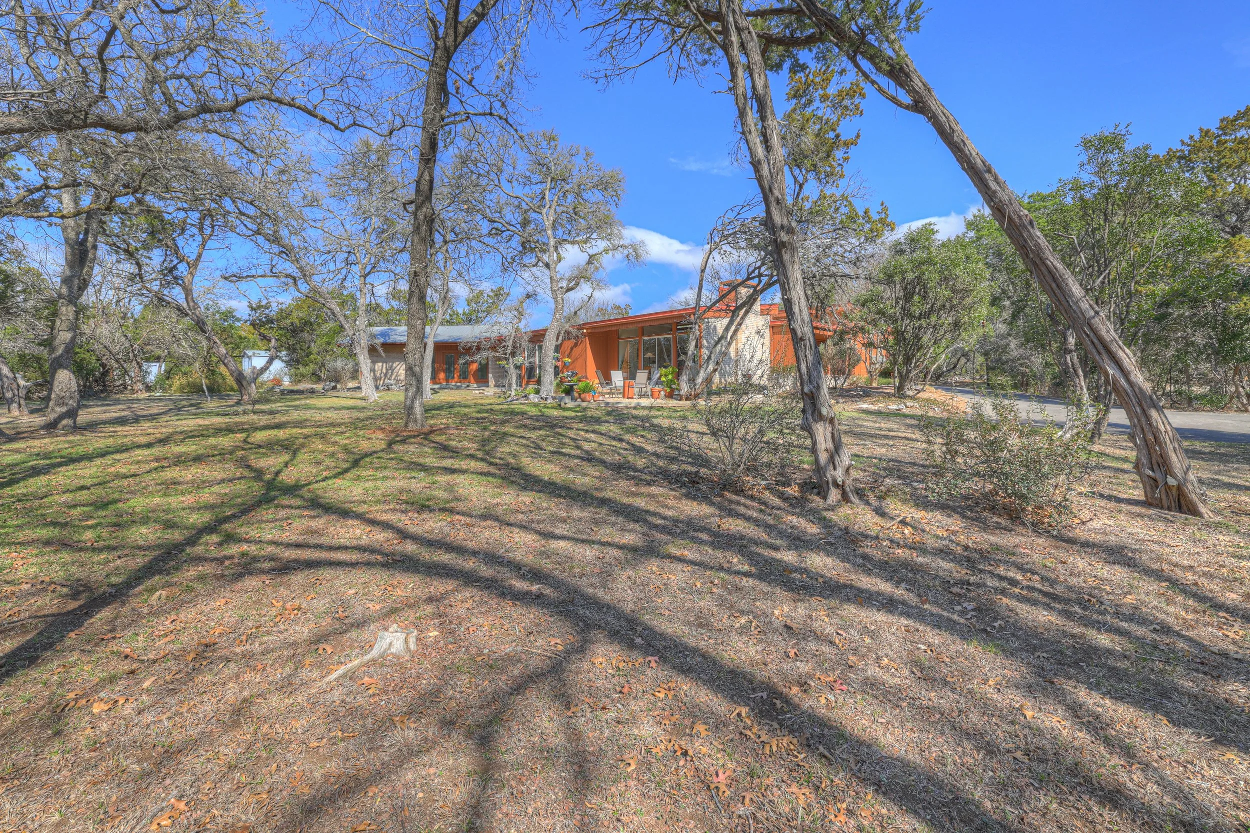 A house with large windows and a porch sitting area, surrounded by trees with long shadows, under a bright blue sky.
