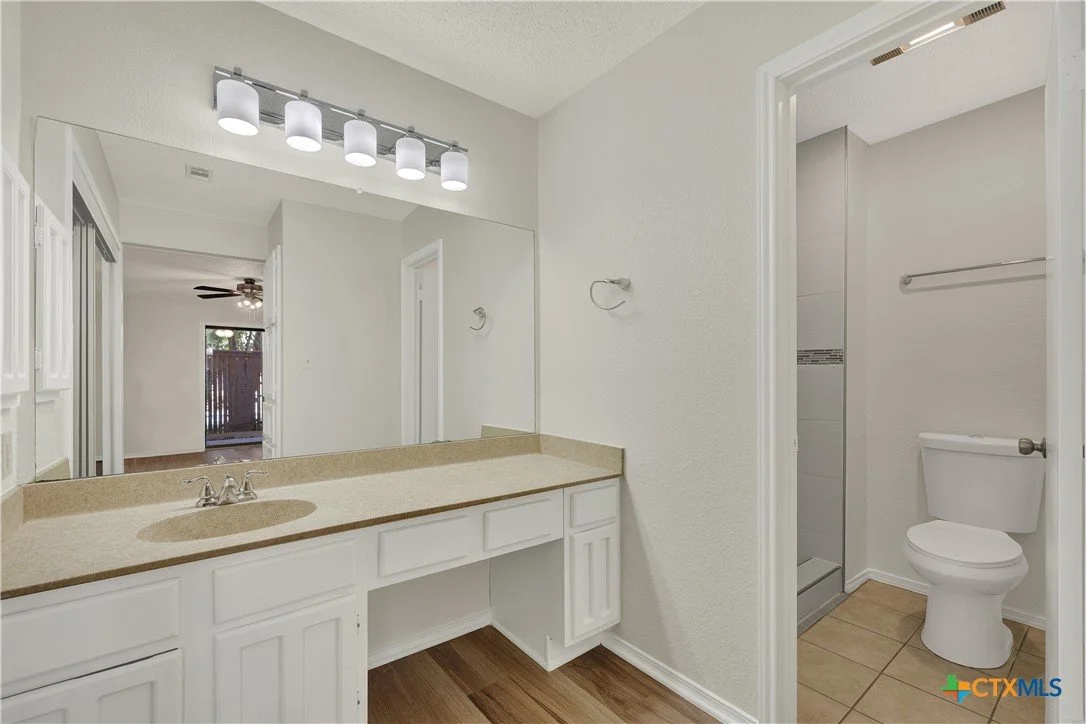 Bathroom vanity with large mirror, four-light fixture, and a separate toilet and shower room with tiled floor.