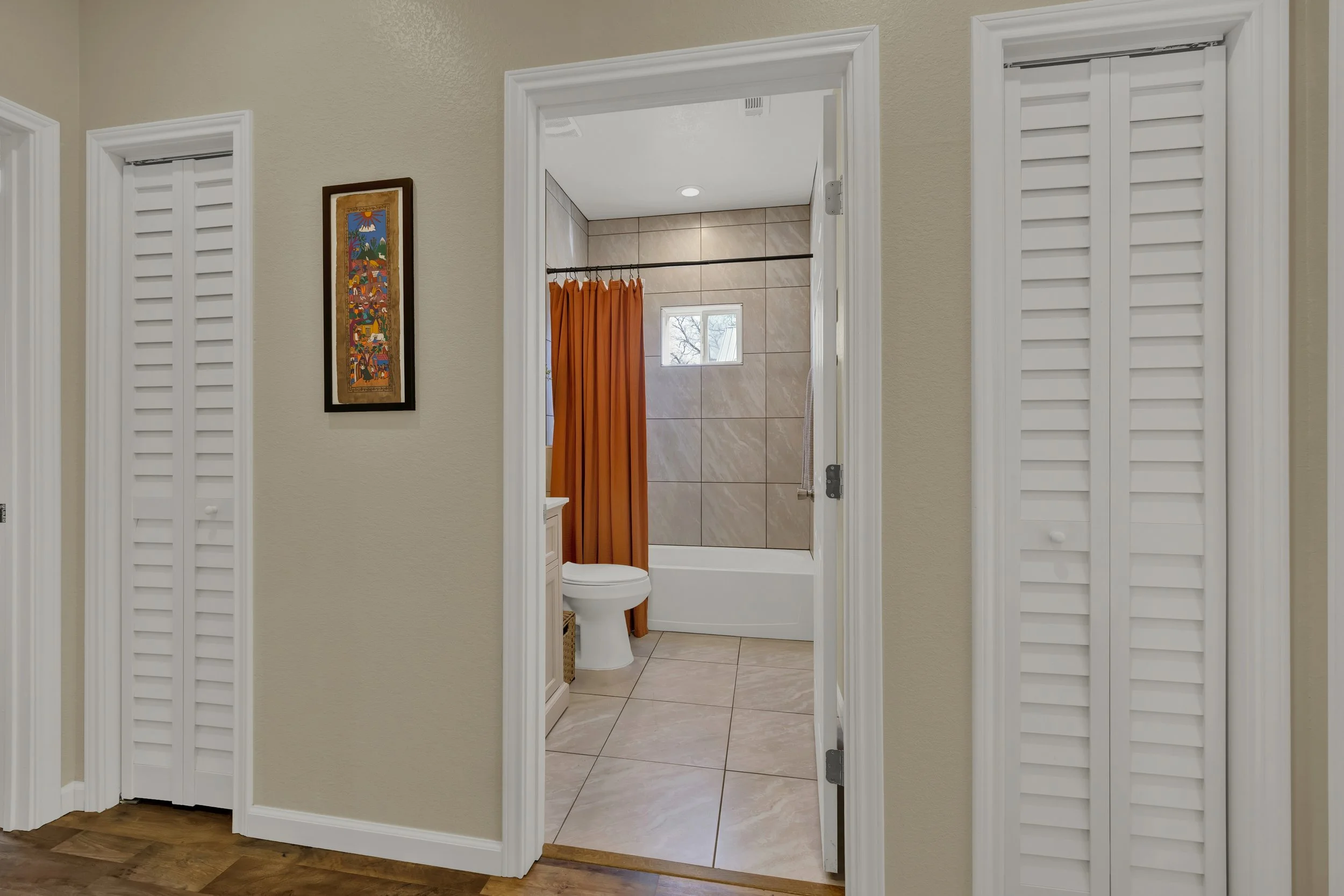 View of a bathroom through an open doorway, with beige walls, a white bathtub, orange shower curtain, small window, and tiled walls.