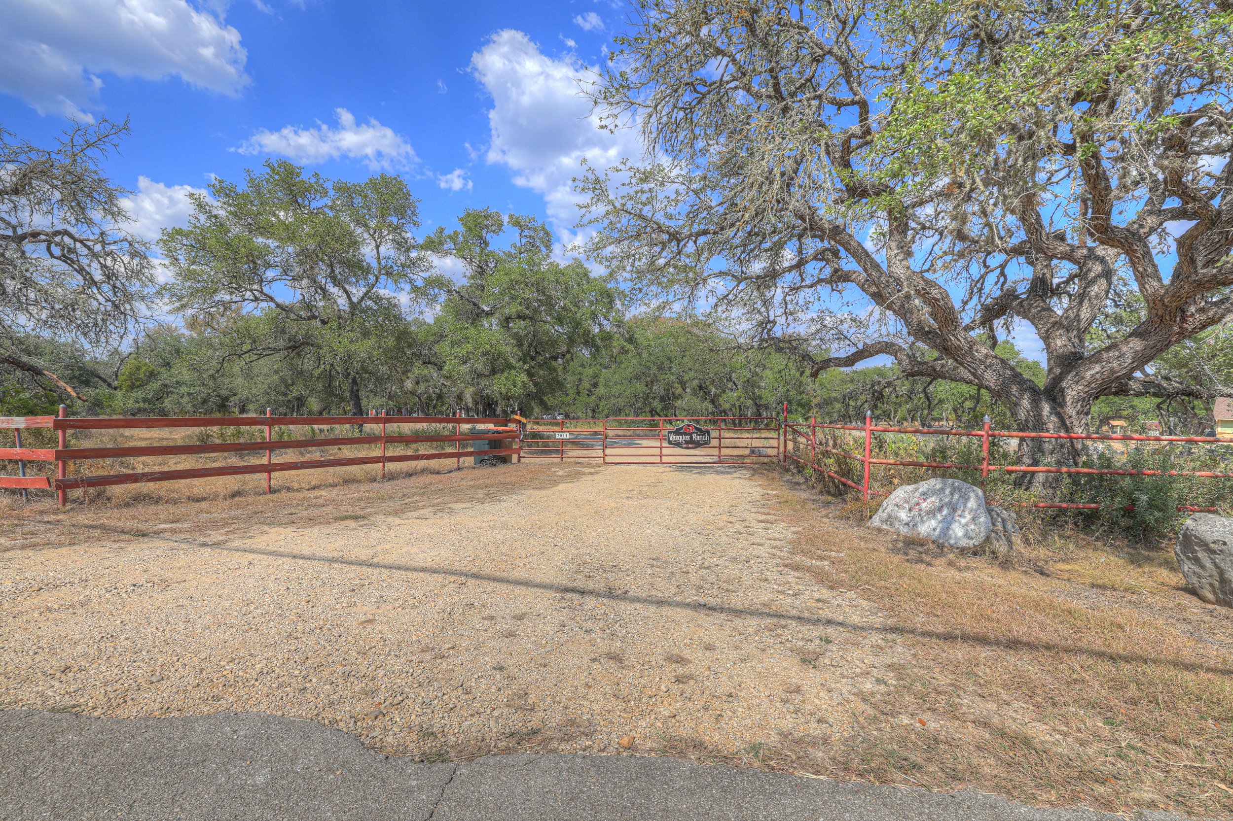 Entrance to Vantage Ranch with a red gate, surrounded by trees and rocks, under a blue sky with scattered clouds.