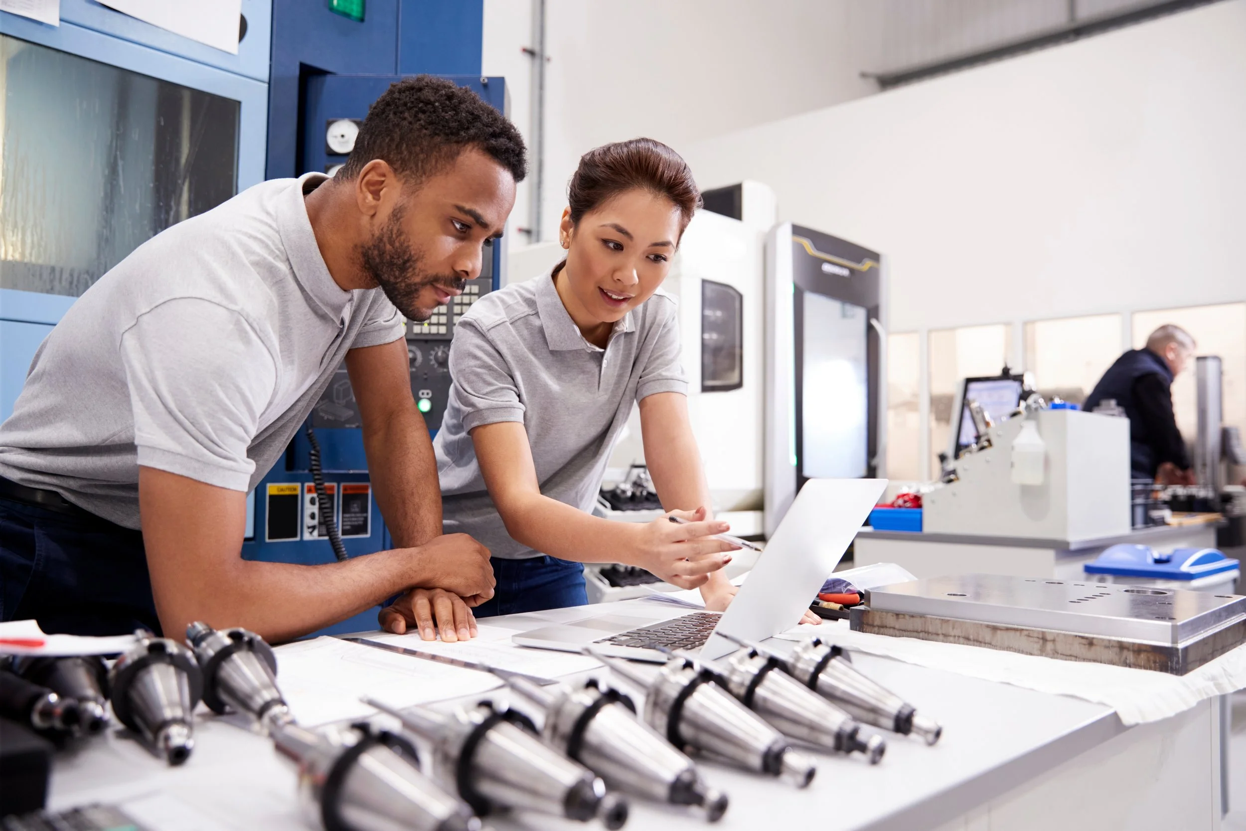 Two engineers in a laboratory are examining a laptop screen, with various mechanical parts, including drill chucks, laid out on the table in front of them. They are focused and discussing their work.