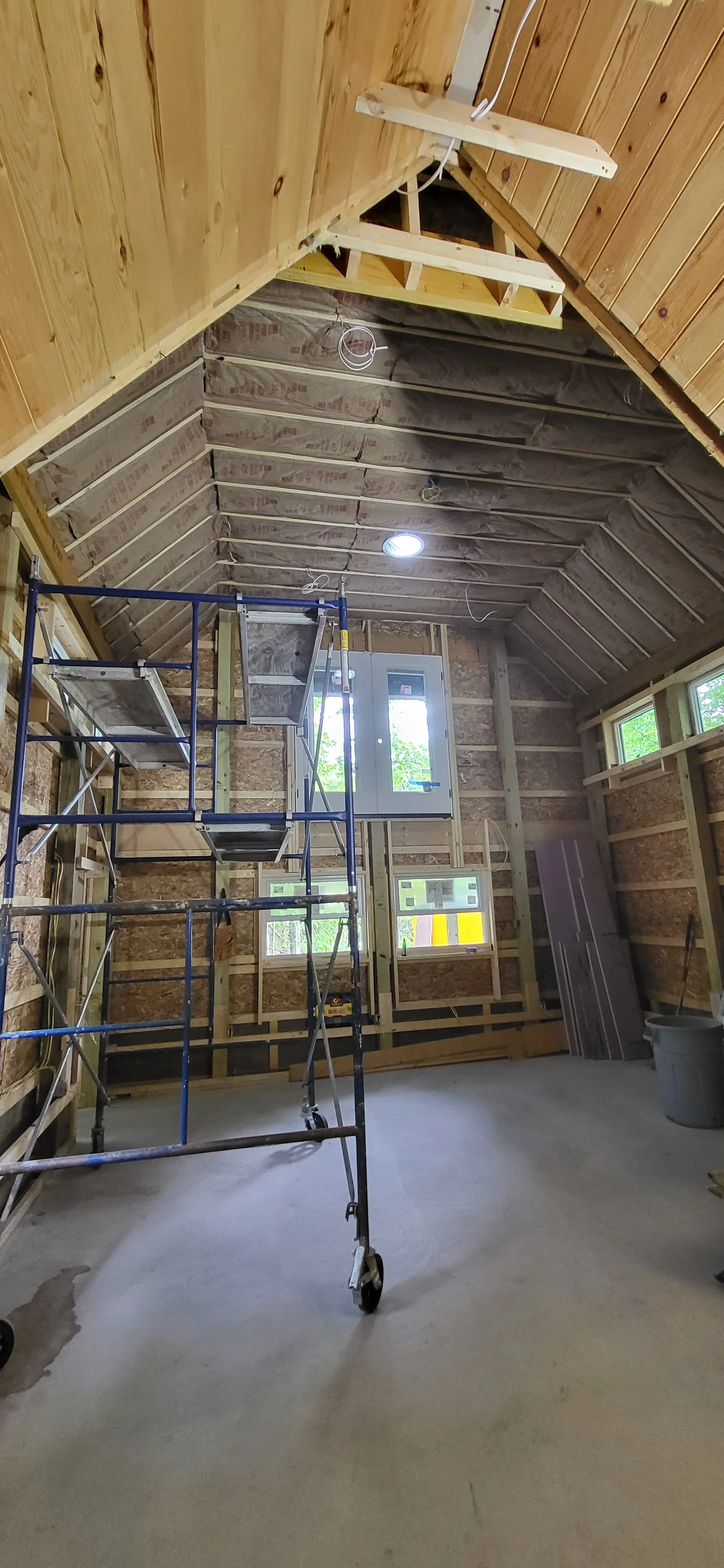 Interior of a room under construction with exposed wooden beams, insulation, windows, and scaffolding. Custom framing in Northern Michigan. Quality Building. Trusted Builder in Northern Michigan. Licensed and Insured builder in Michigan.