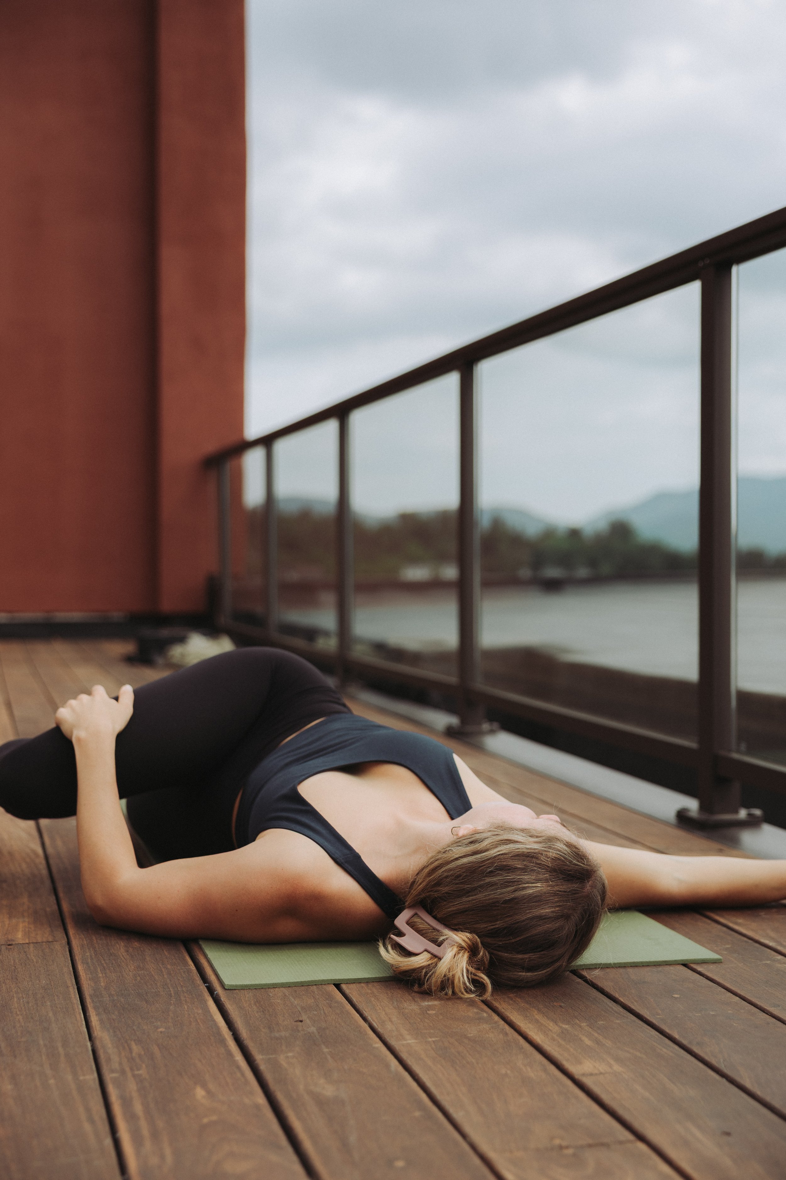 Woman doing a side stretch on a yoga mat on a wooden deck, overlooking a cloudy sky and mountains in the distance.