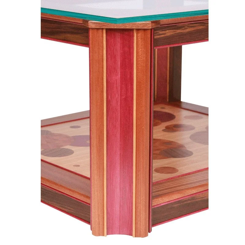 Close-up of a wooden table with a glass top and a lower shelf with a colorful, patterned surface.