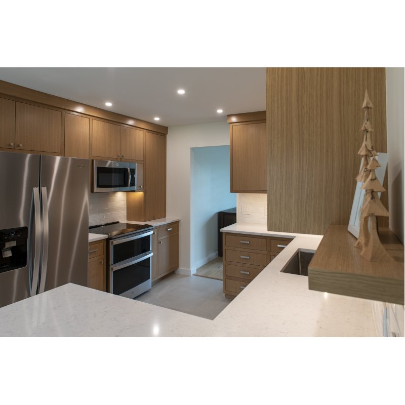 Modern kitchen with wooden cabinets, stainless steel appliances, including a refrigerator, microwave, and oven, and a white countertop with a small wooden decorative tree.