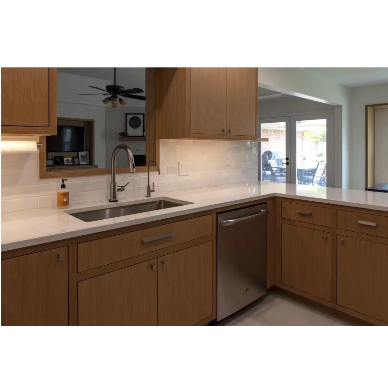 Kitchen with wooden cabinets, white countertop, and stainless steel sink, showing a sliding glass door leading outdoors.