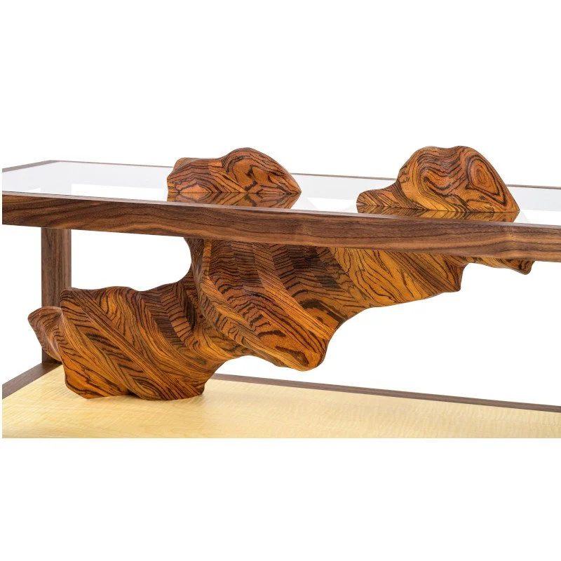 A modern wooden table with an artistic base made from sculpted wood, topped with a glass surface.