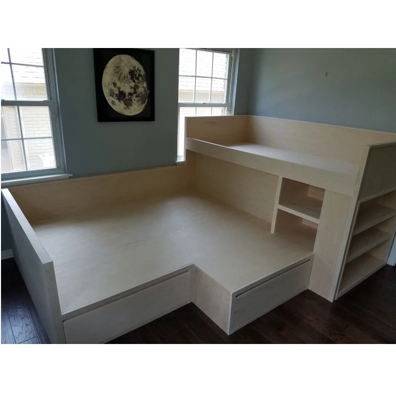 unfinished custom wooden bed frame with storage shelves in a brightly lit bedroom with two windows and a moon poster on the wall