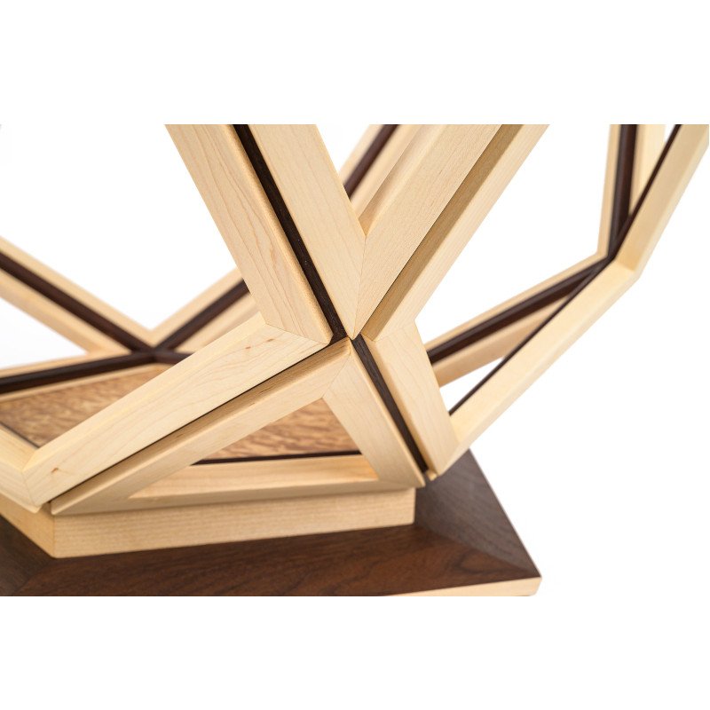Close-up of a wooden geometric coffee table with interlocking light and dark wood pieces, resting on a dark wooden base.