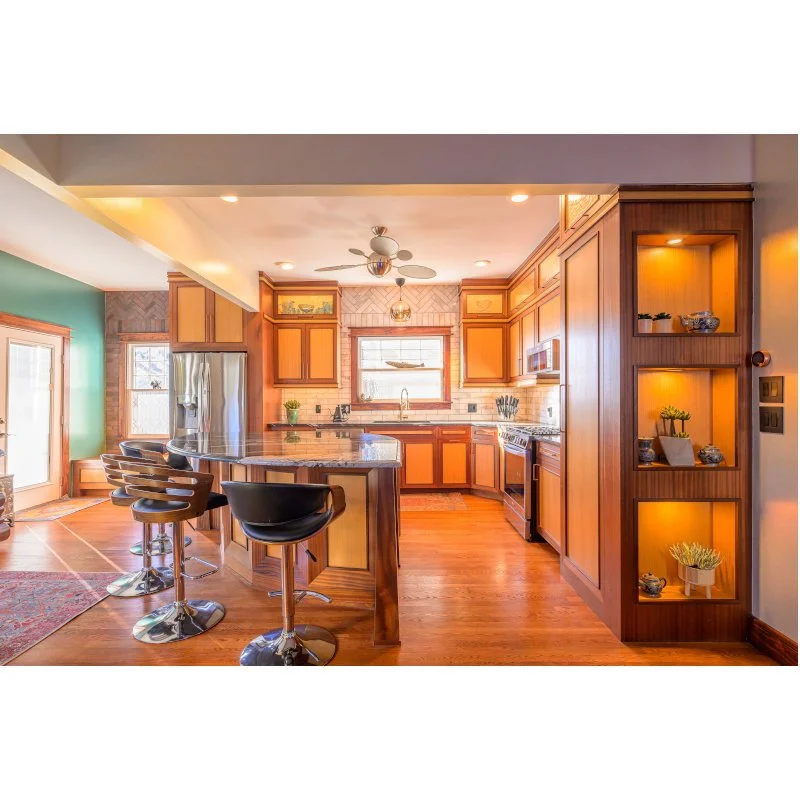 Kitchen with wooden cabinets, a granite countertop island, black bar stools, stainless steel appliances, a window above the sink, and built-in shelves with decorative items.