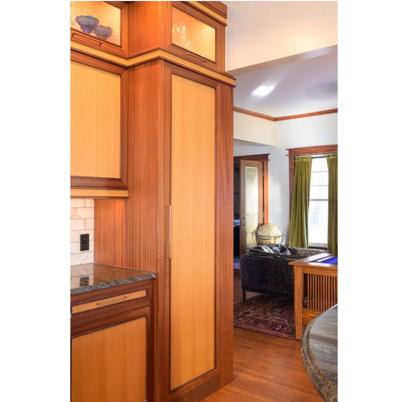 A view of a living room with wooden cabinets, green curtains, a black sofa with pillows, a globe on a side table, and a doorway leading to another room.