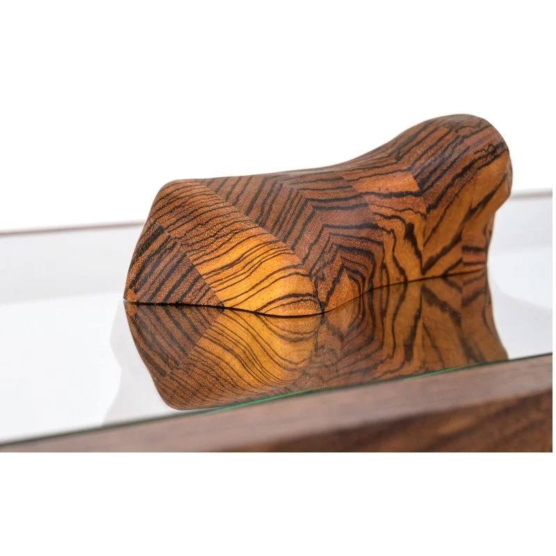 Close-up of a wooden sculpture with a smooth, rounded shape and intricate grain patterns, reflecting on a glass surface.