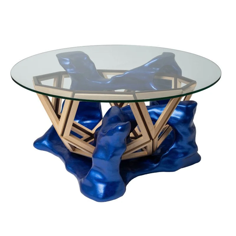 Modern coffee table with a glass top, wooden geometric base, and irregular blue sculptural elements.