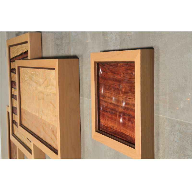 Close-up of two wooden art pieces mounted to grey tiled wall.