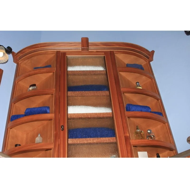Wooden bathroom cabinet with curved shelves, blue towels, and various small bottles and containers, mounted on a blue wall.