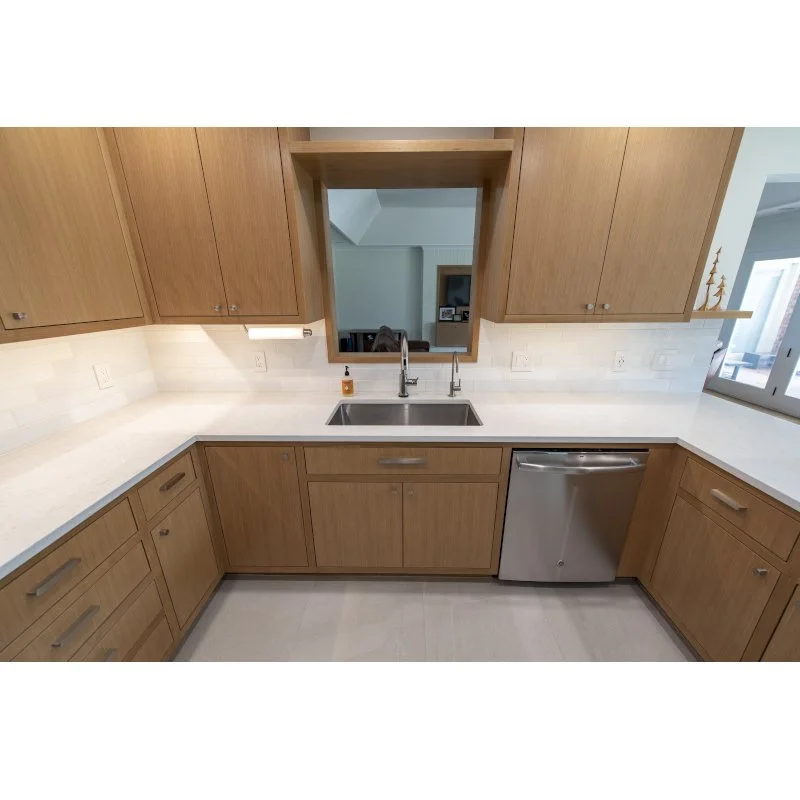 Kitchen with wooden cabinets, white countertops, stainless steel sink, and dishwasher. There is a window on the right and a reflection showing part of the living area.
