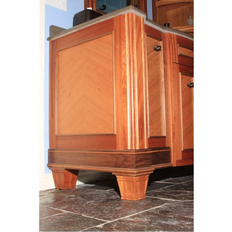 Close-up of a wooden kitchen cabinet with decorative legs, corner view showing wood grain and cabinet handles.