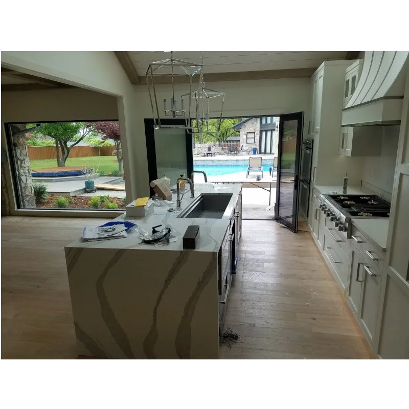 Modern kitchen with white cabinetry, marble island, and view of backyard swimming pool and outdoor seating area.