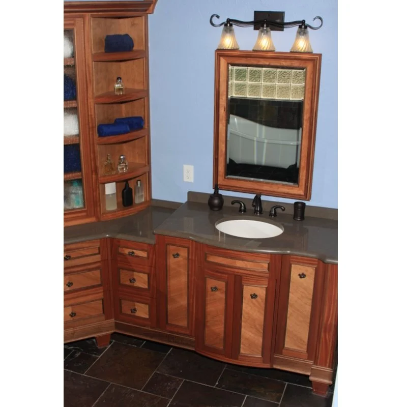 Bathroom vanity with a wooden cabinet, a mirror with a wooden frame, three small lights above the mirror, a dark faucet, and a granite countertop.