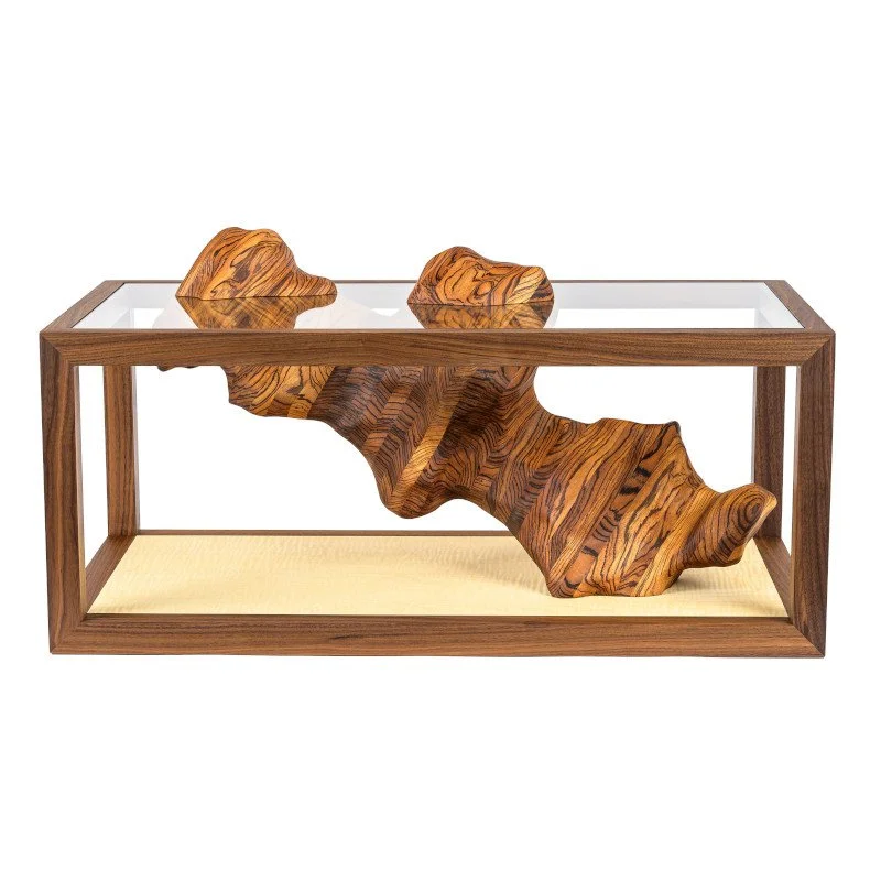 A custom wooden coffee table with a floating zebra wood sculpture with glass passing through it.