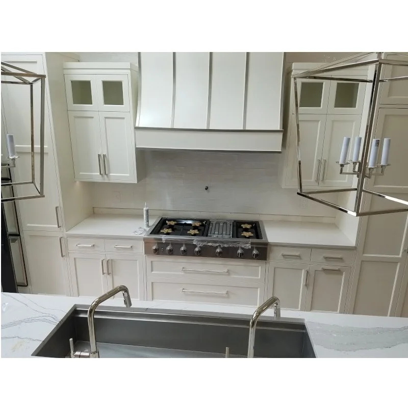 Modern white kitchen with stainless steel stove, white cabinets, and pendant lighting fixtures.
