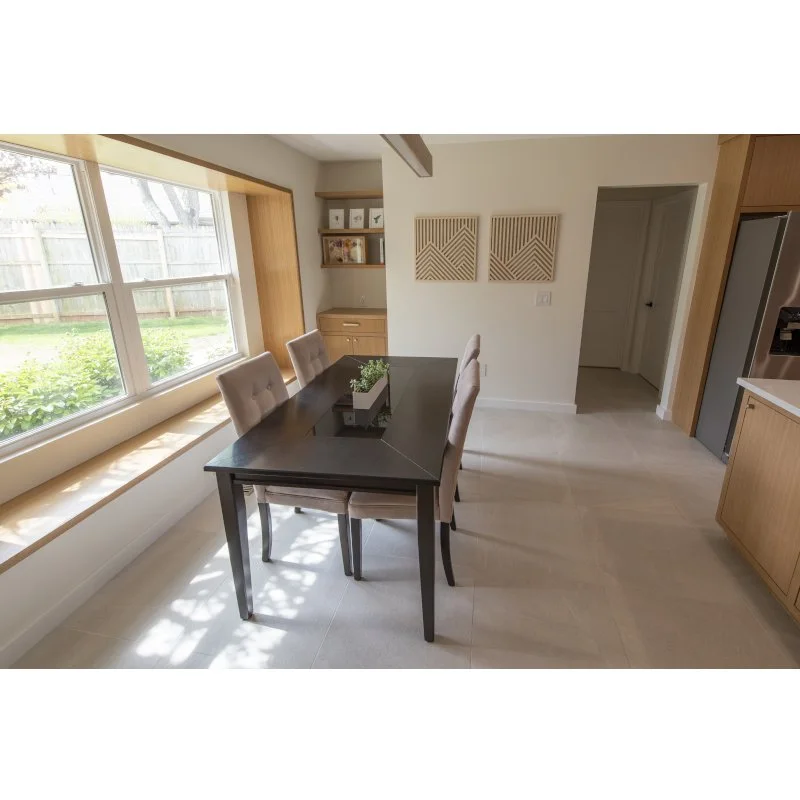 Dining room with a black table, four beige upholstered chairs, large window with a window seat, and wooden wall accents.