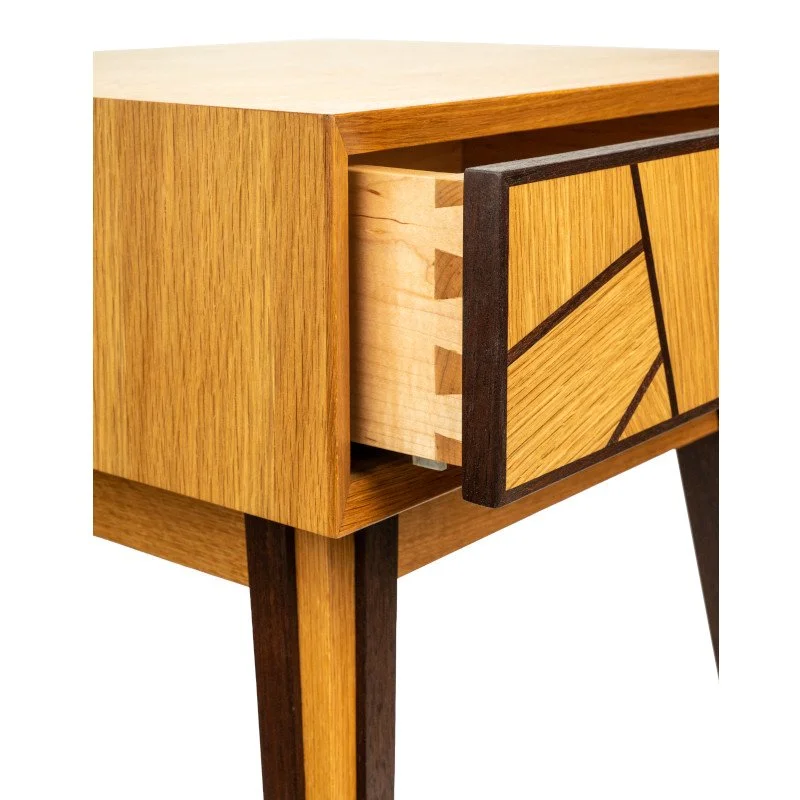 A wooden mid-century modern style side table with an open drawer and geometric pattern on the drawer front, featuring a mix of light and dark natural woods.