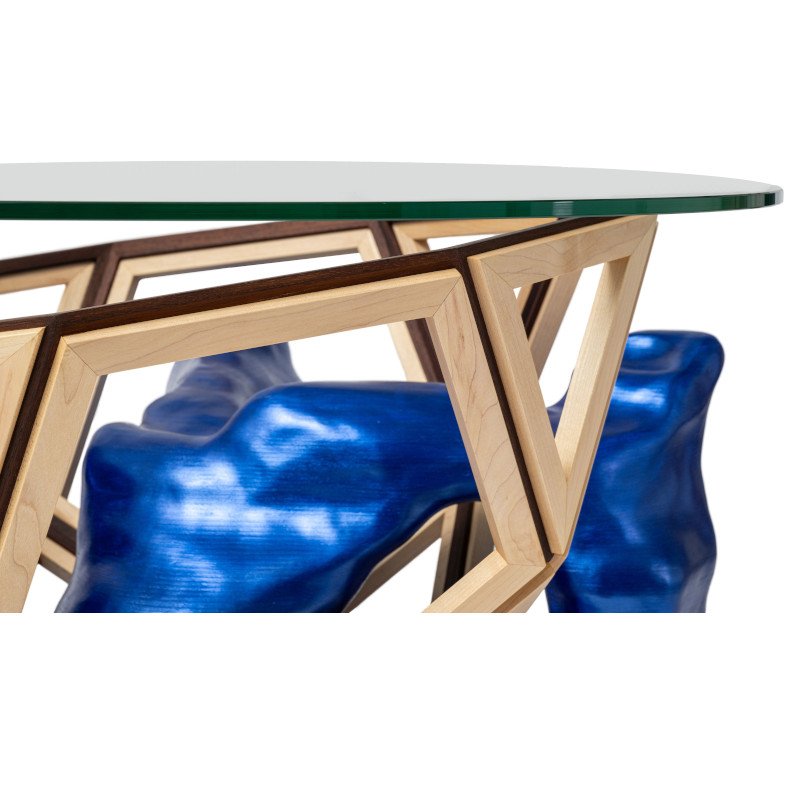 Close-up of a modern glass-top table with wooden geometric base and a blue sculpture.