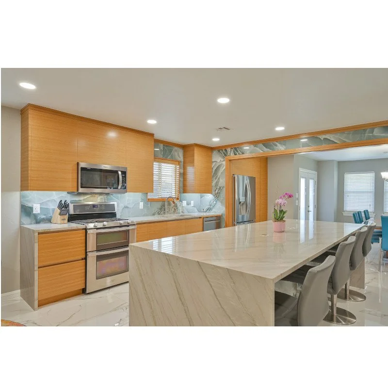Modern kitchen with wooden cabinets, stainless steel appliances, quartzite countertops, and a large island with waterfall ends and bar stools.