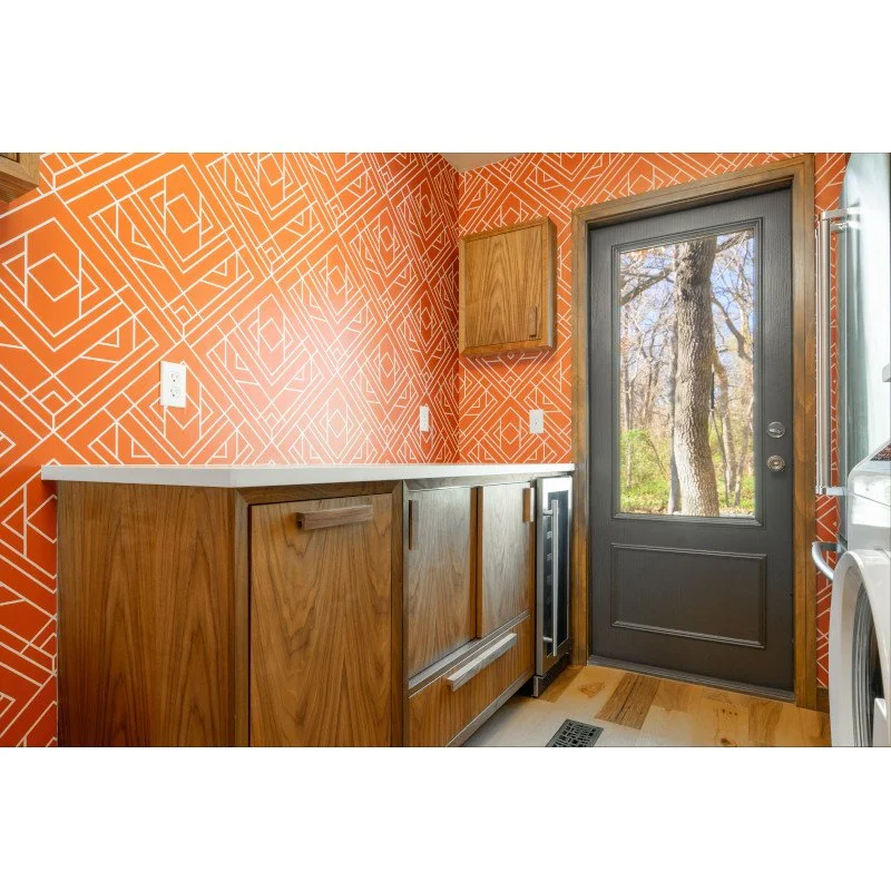 Laundry room with orange patterned wall paper, wooden cabinetry, a gray door with glass window, and a washer and dryer.