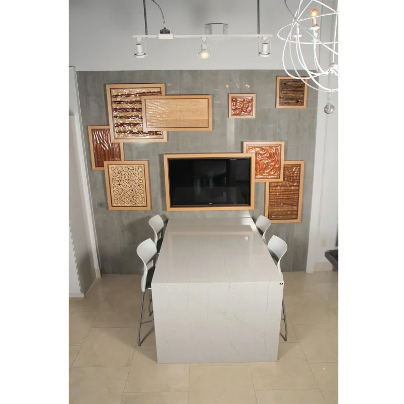 Conference meeting area with a white marble table, four white chairs, a wall decorated with various wooden framed art pieces, and a large flat-screen TV mounted on the wall.