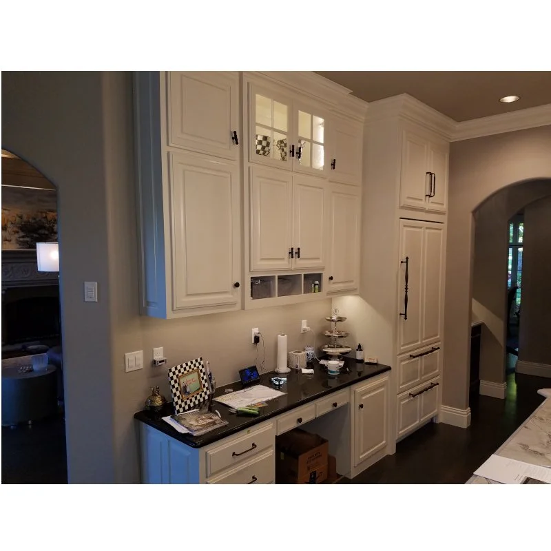 A kitchen with white cabinets, black countertop, and various small appliances and decor on the counter.